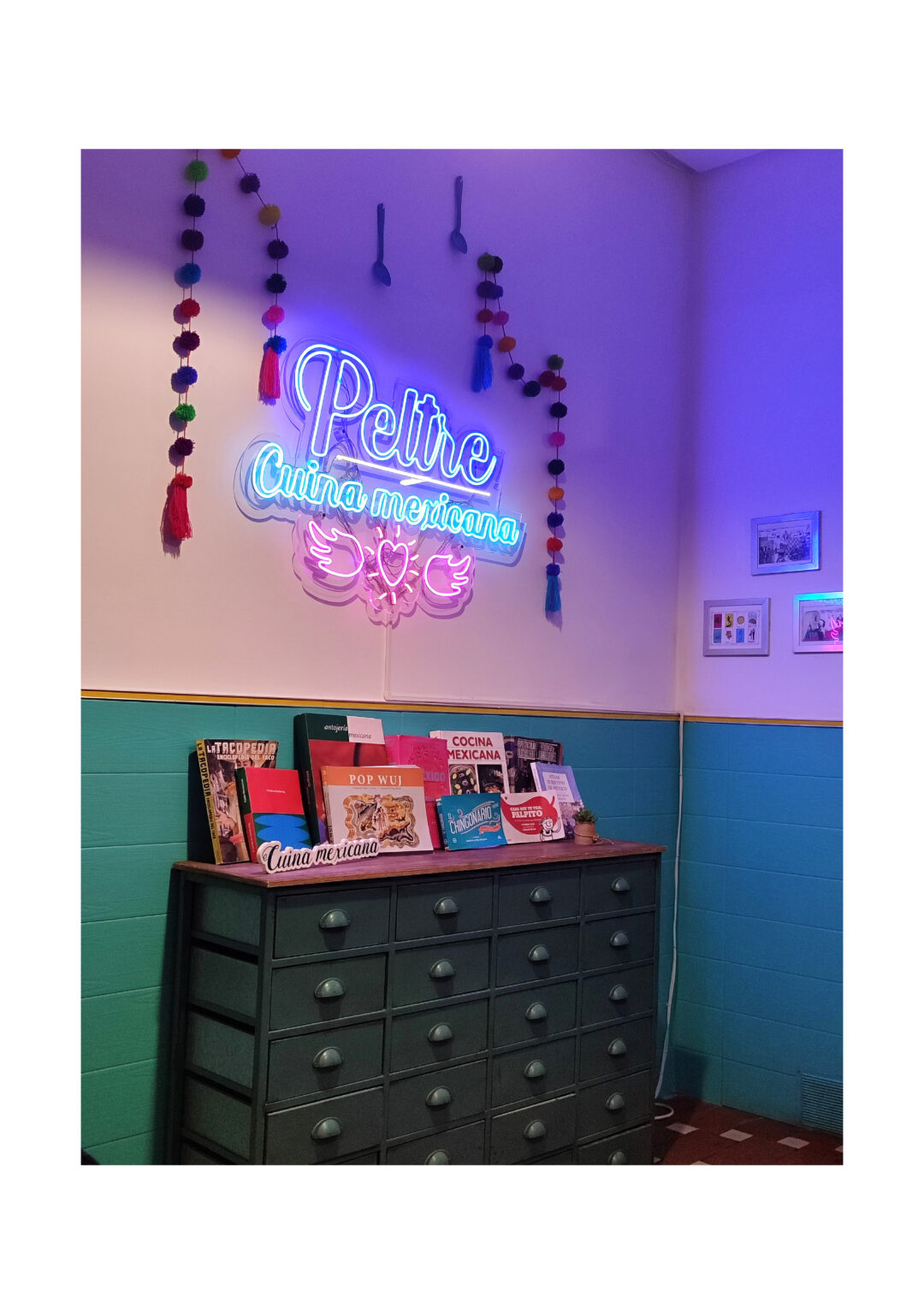 Neon 'Petite Cuina Mexicana' sign above cookbook display