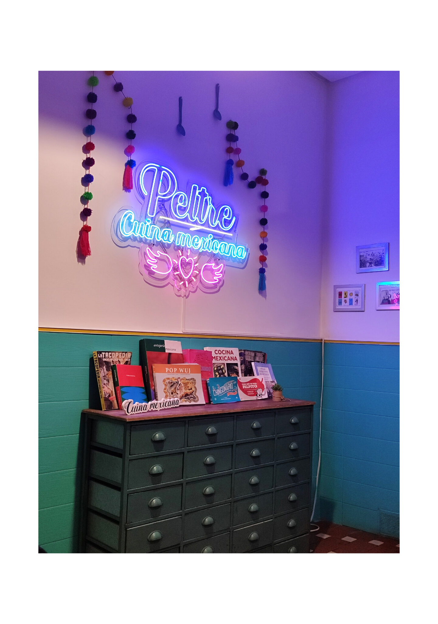 Neon 'Petite Cuina Mexicana' sign above cookbook display