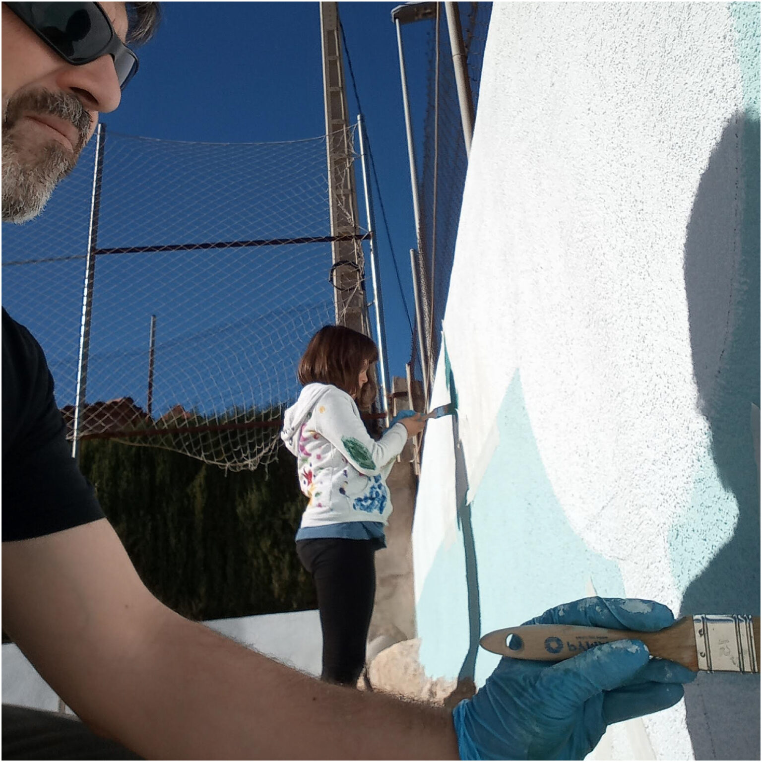 Man and child painting outdoor wall blue