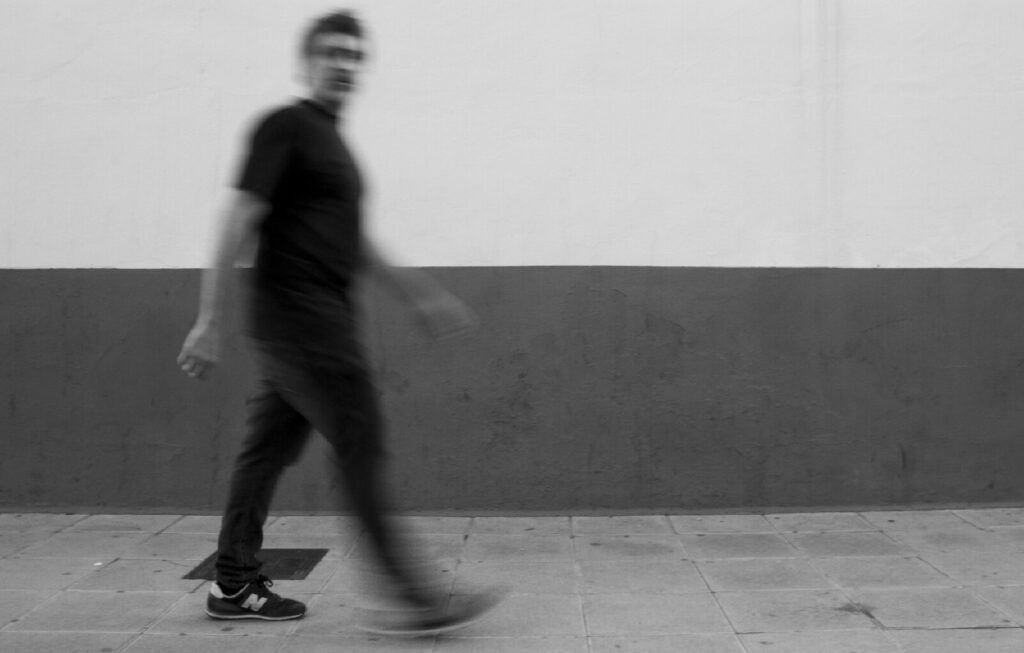 Blurred man walking past plain wall in black and white